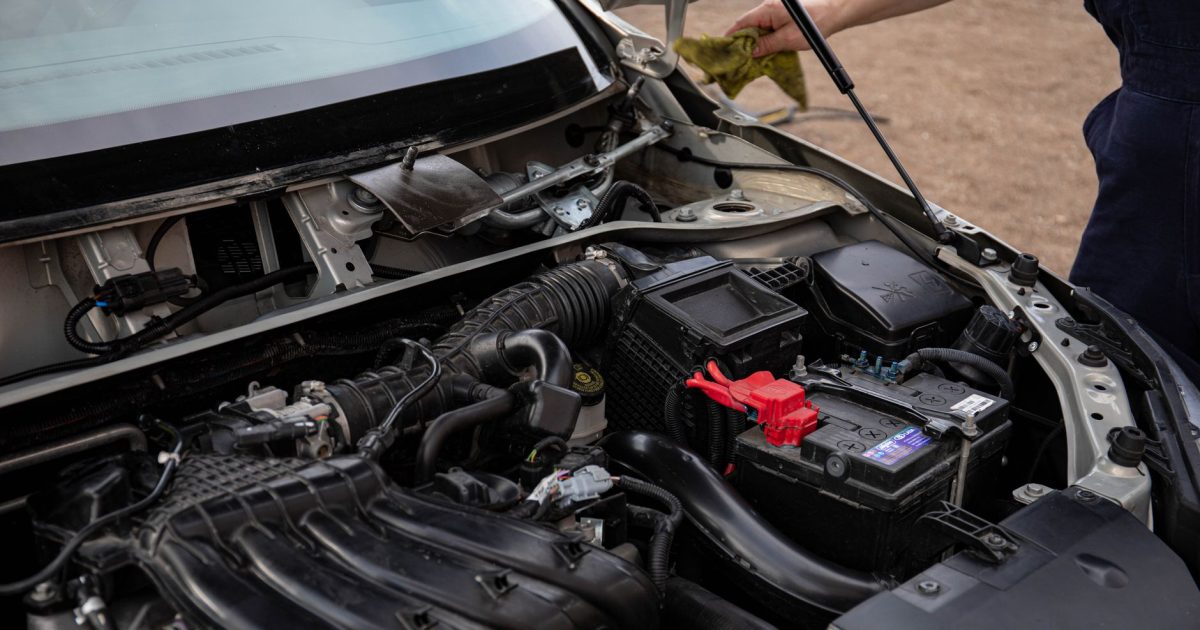 Mechanic inspecting car engine bay and battery during routine maintenance.