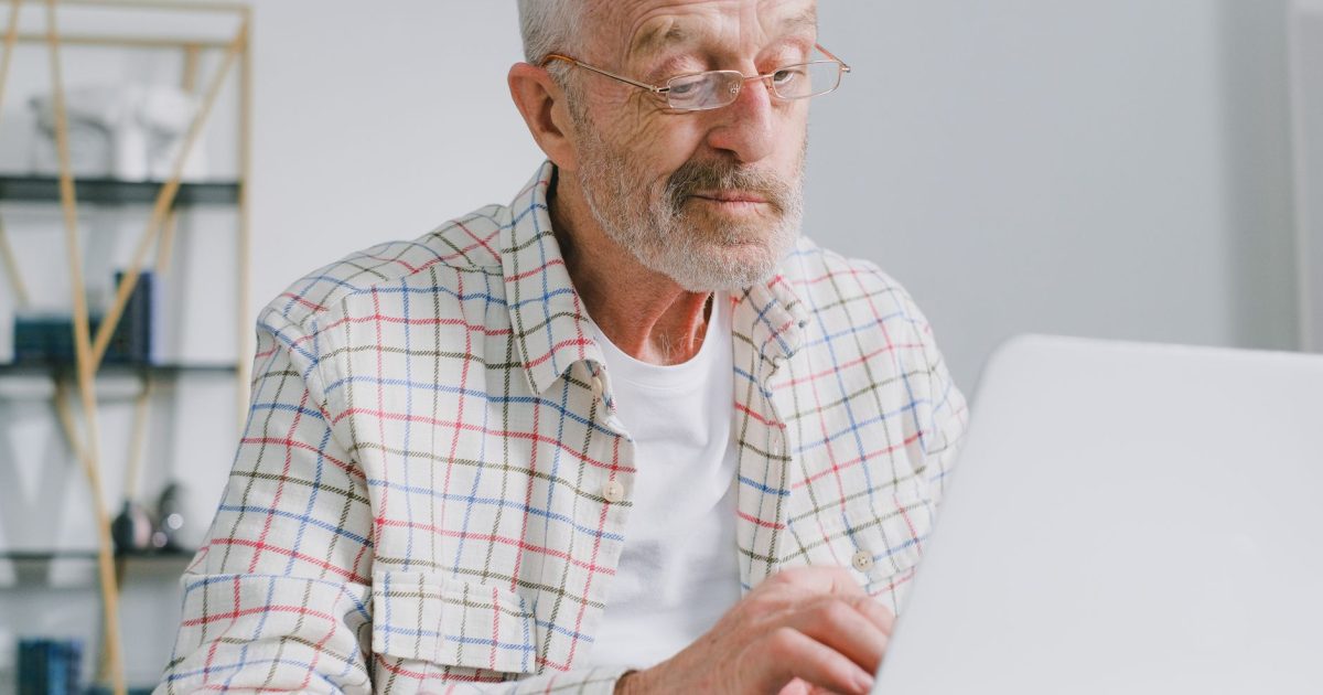 Senior man with eyeglasses working on a laptop in a modern indoor setting.