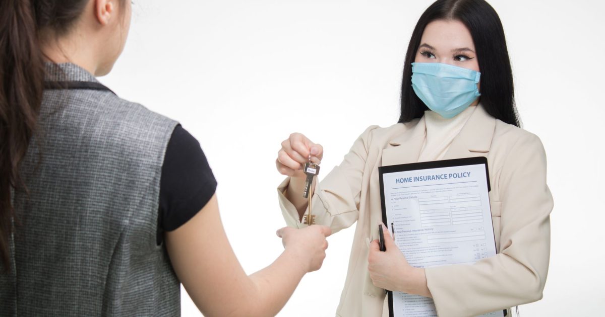 Real estate agent in a face mask hands keys to a client, illustrating safe business practices.