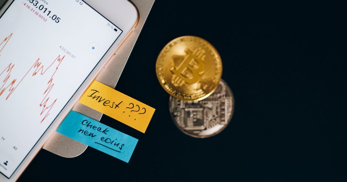 Bitcoin coins and smartphone displaying price chart with investment notes.
