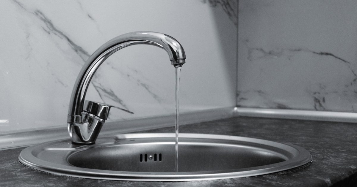 Chrome faucet with running water in a modern kitchen with marble countertop.