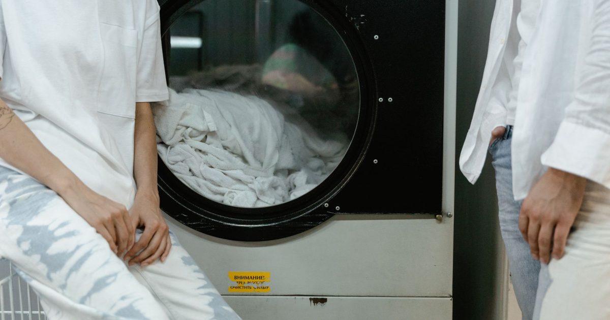 Adults in white clothes using a washing machine in a laundry facility.
