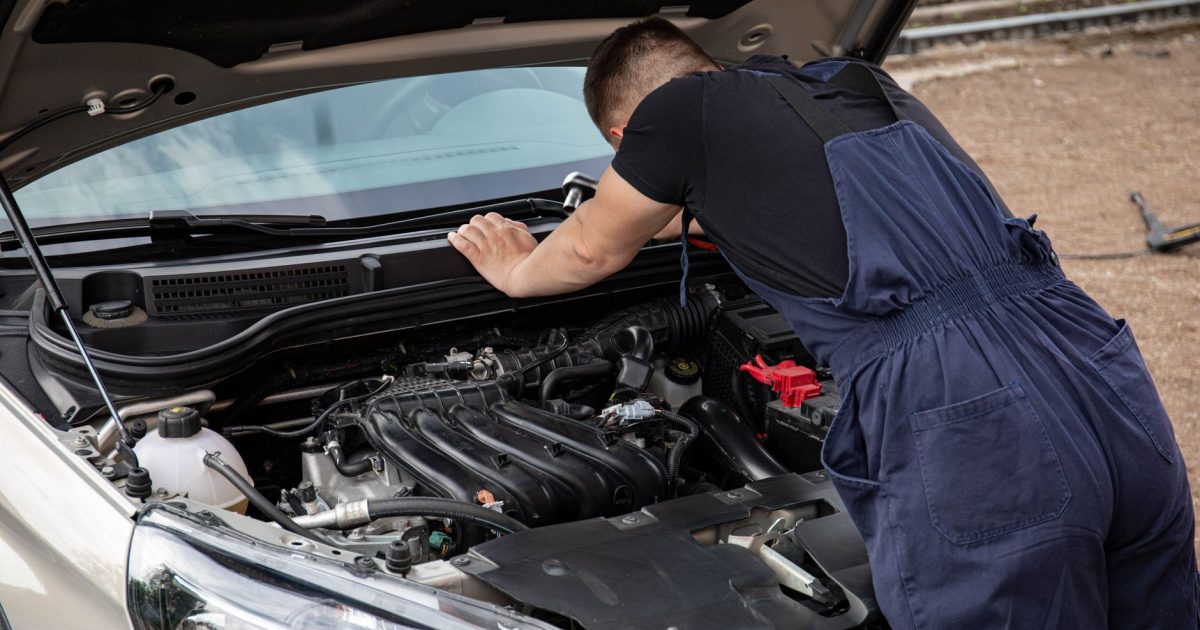 Mechanic checking car engine outdoors, focusing on vehicle maintenance and repair.