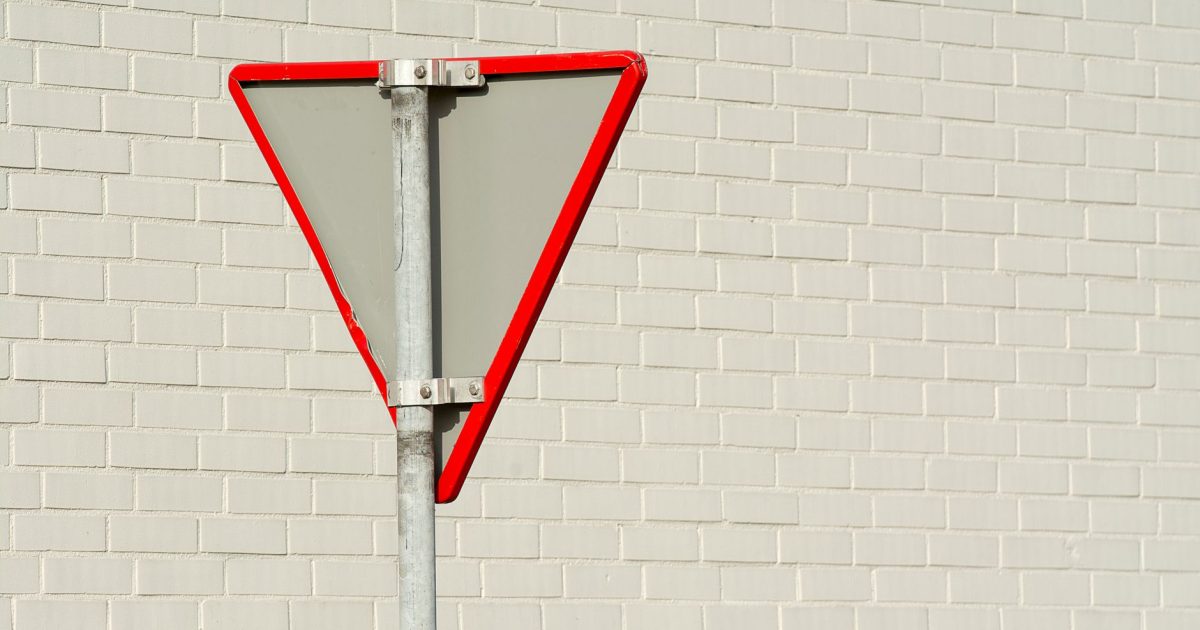 Simple yield sign on a white brick wall offers a minimalist urban aesthetic.
