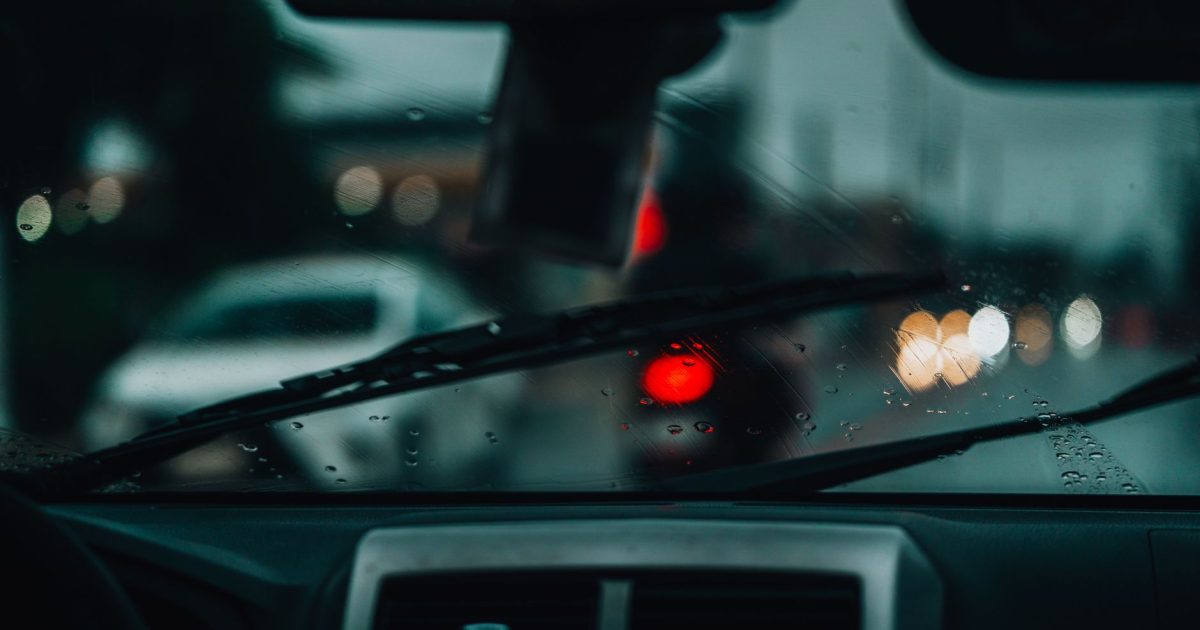 Raindrops on windshield with blurred city lights and cars, creating a moody urban scene.
