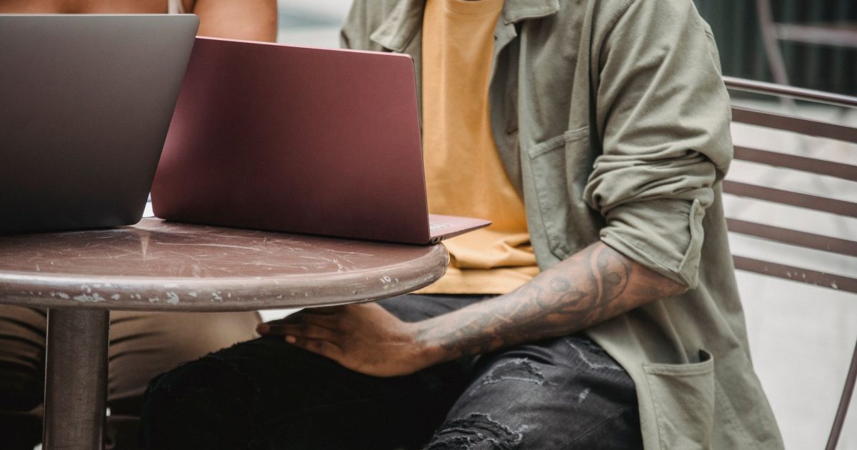 Crop anonymous multiracial man and woman sitting at round table with laptops while working remotely together on startup in cafe