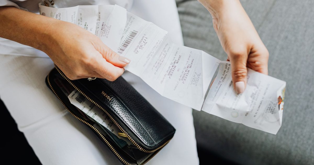 Close-up of a woman's hands managing multiple receipts taken from a black wallet.
