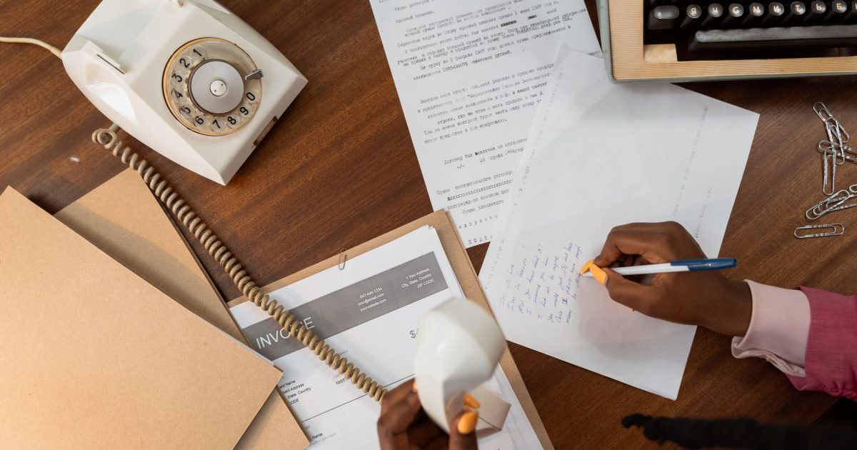 Overhead view of a person writing notes while holding a vintage telephone on a wooden desk.
