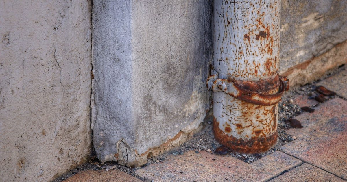Close-up of a rusty metal pipe attached to an old, weathered wall.