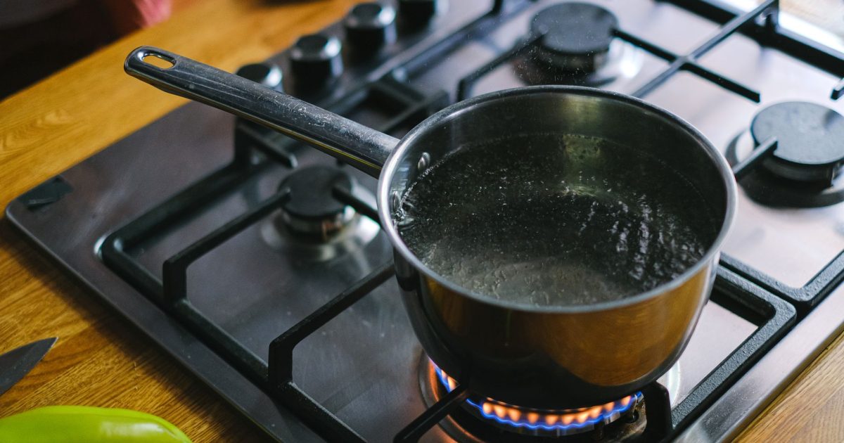 Close-up of boiling water in a stainless steel pot on a gas stove in a kitchen setting.