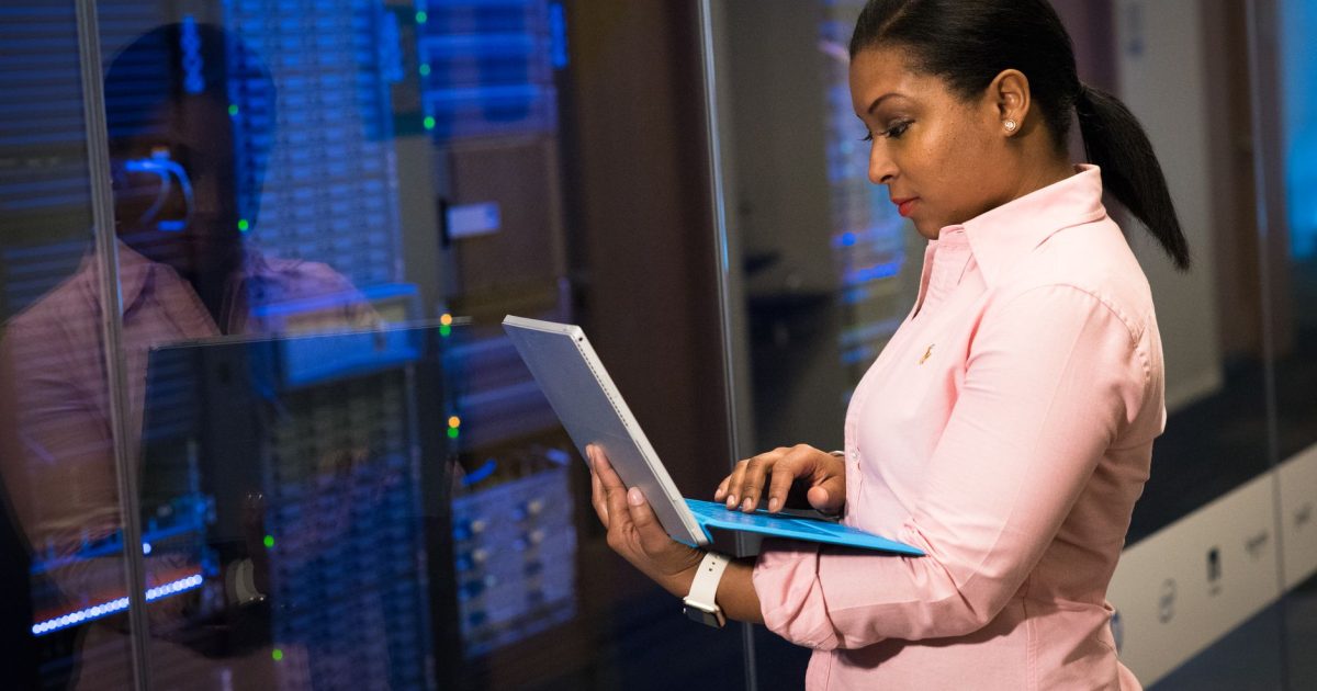 A focused software engineer working on a laptop in a server room, reflecting dedication in tech.