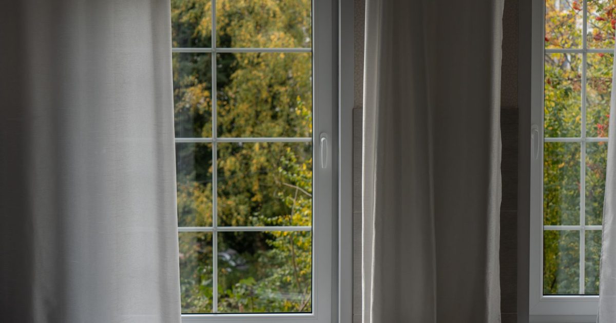 Serene interior with white curtains framing a lush green outdoor view through a window.