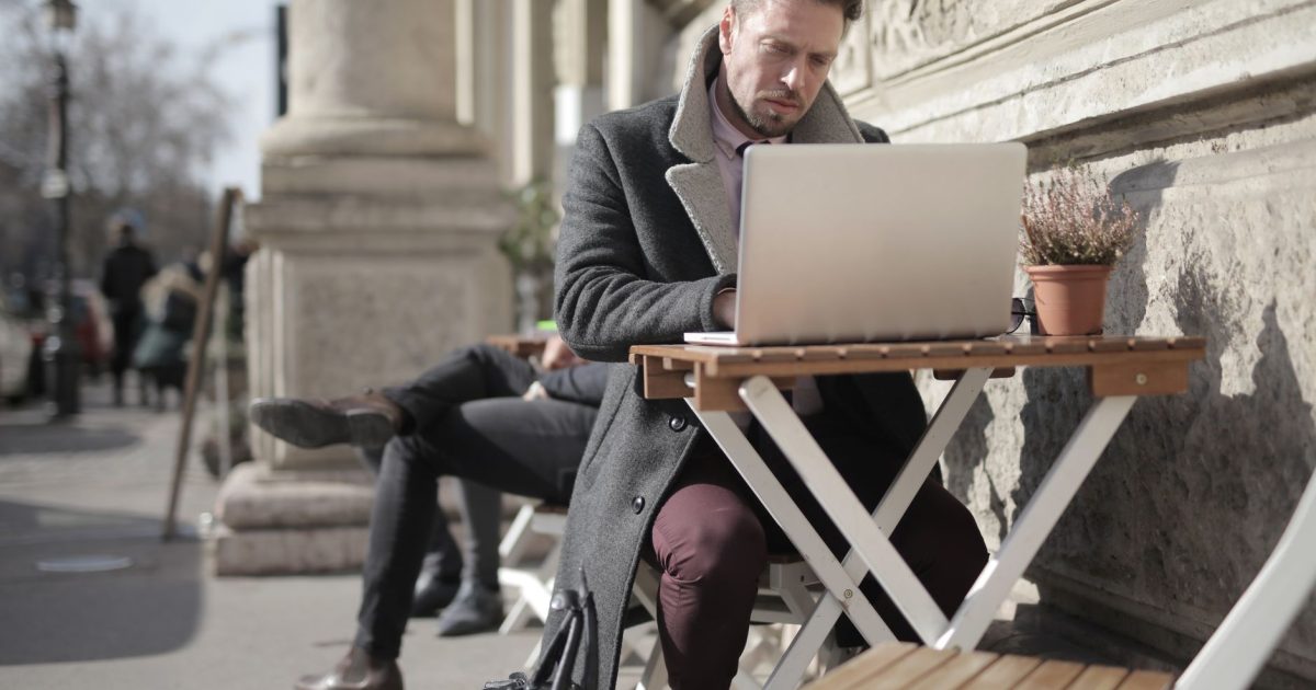Freelancer working on laptop outdoors in urban area, embracing remote work lifestyle.