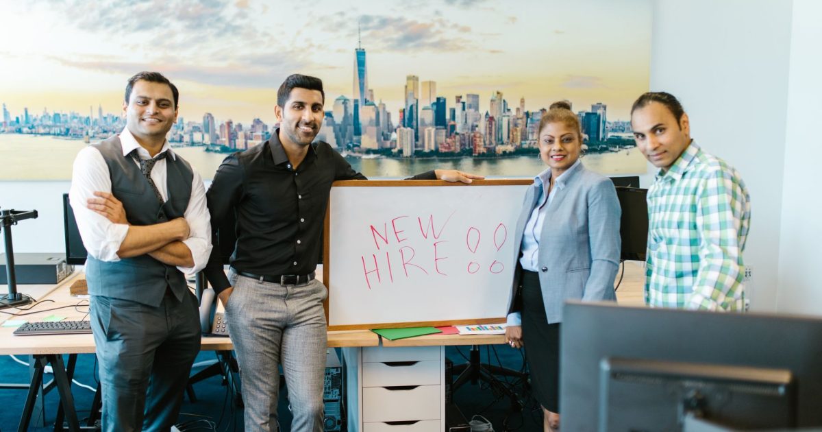 Diverse team standing with 'New Hire' sign, symbolizing collaboration and teamwork.