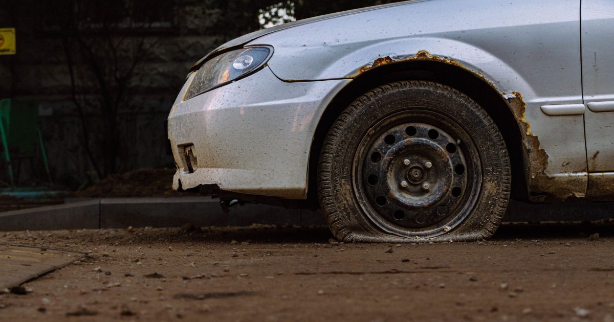 Close-up of a rusted car with a flat tire parked on a street in Moscow, illustrating urban decay.